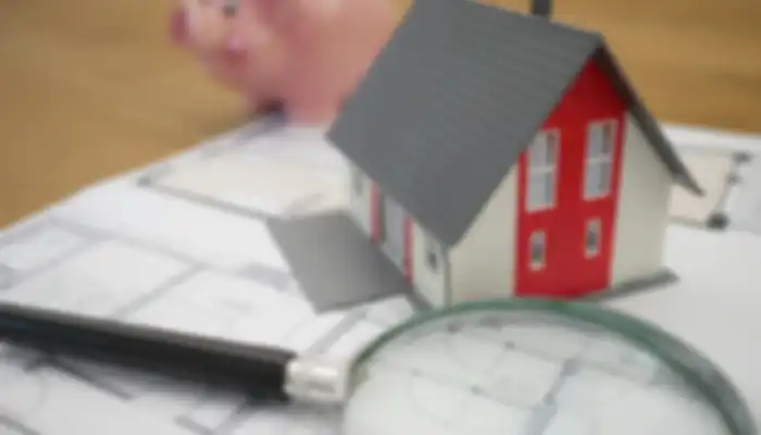 House, piggy bank, magnifying glass sitting on blueprints